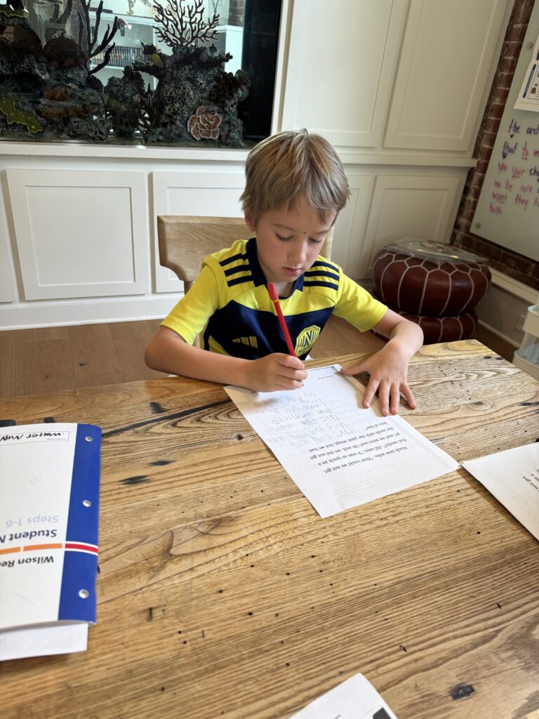 Young student writing on a paper at a wooden table during a tutoring session.